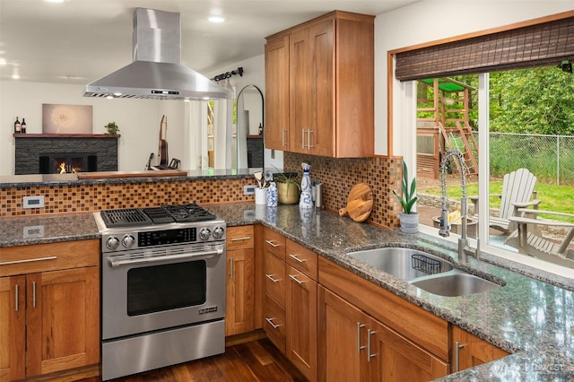 kitchen featuring a sink, stainless steel range with gas stovetop, brown cabinetry, wall chimney exhaust hood, and tasteful backsplash