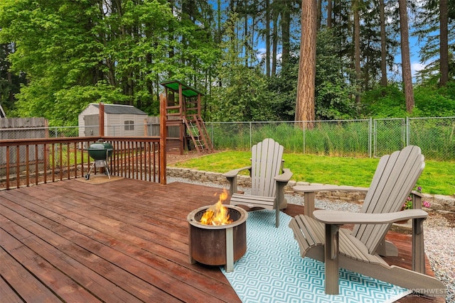 deck with a shed, a fenced backyard, a playground, an outdoor structure, and a fire pit