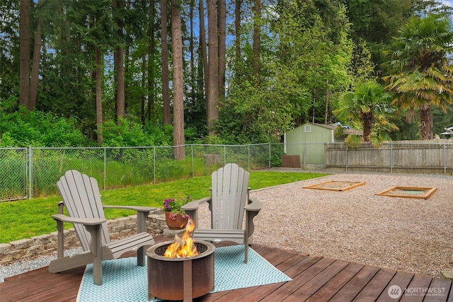 wooden deck featuring a fenced backyard, an outdoor fire pit, a shed, and an outbuilding