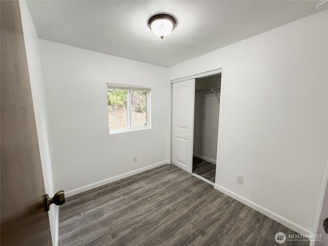 unfurnished bedroom with a closet, baseboards, and dark wood-type flooring