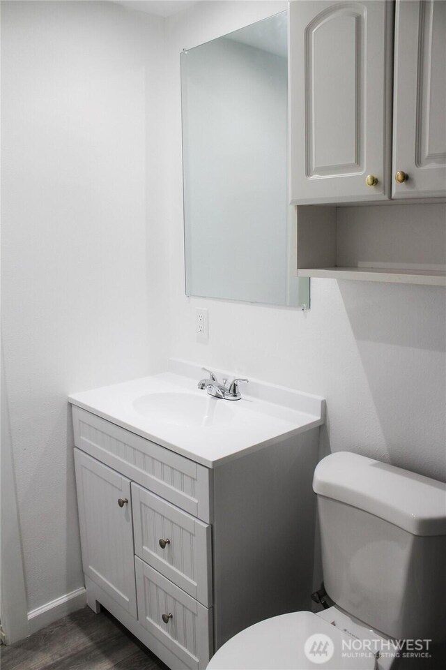 bathroom with vanity, baseboards, wood finished floors, and toilet