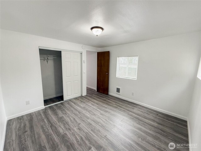 unfurnished bedroom with baseboards, a closet, wood finished floors, and visible vents