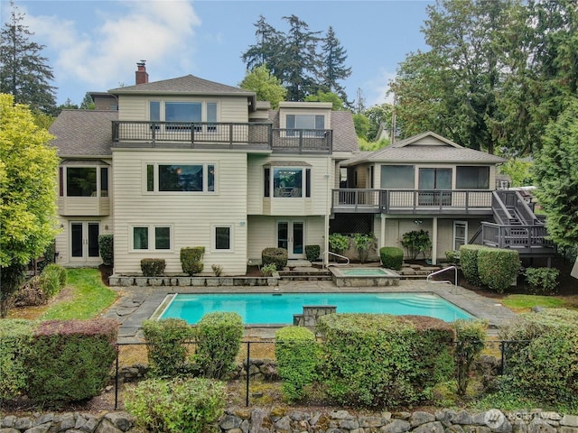 rear view of property featuring an in ground hot tub, french doors, a chimney, an outdoor pool, and a balcony