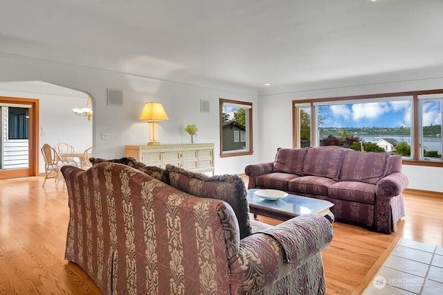 living area featuring light wood-style floors, arched walkways, visible vents, and an inviting chandelier