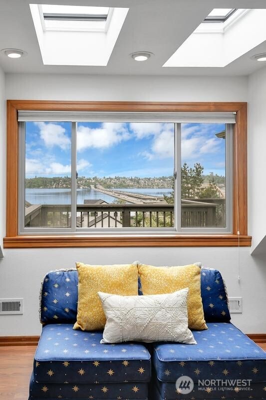 sitting room with baseboards, a water view, a skylight, and wood finished floors