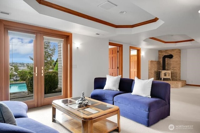 living area featuring crown molding, light colored carpet, a wood stove, a tray ceiling, and visible vents