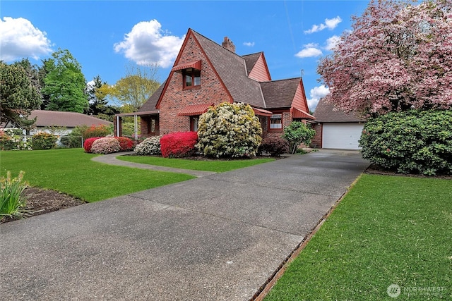 tudor-style house with a shingled roof, a detached garage, a front yard, an outbuilding, and a chimney