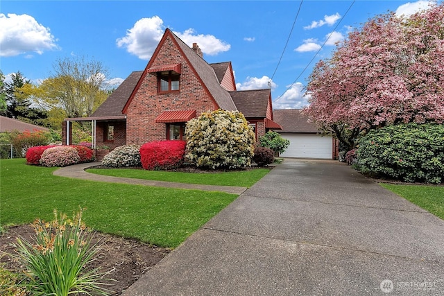 tudor home featuring brick siding, a shingled roof, a front yard, and a garage