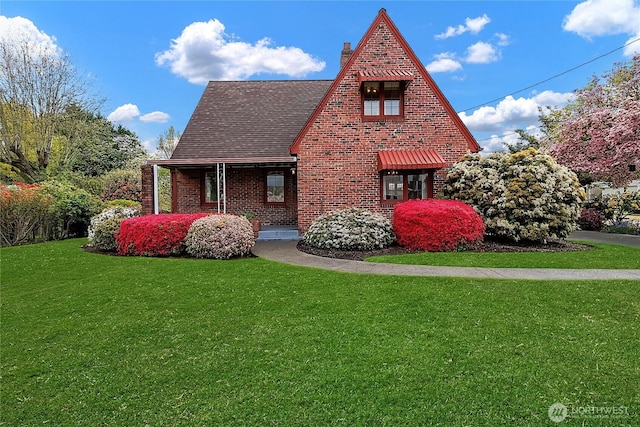 view of home's exterior with a shingled roof, brick siding, a chimney, a lawn, and covered porch
