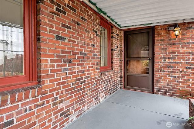 doorway to property featuring a porch and brick siding