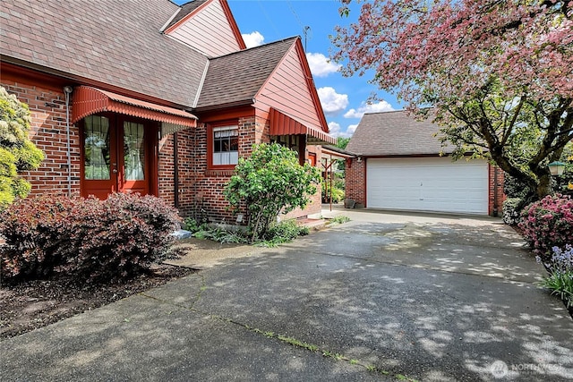 view of side of home with brick siding, a shingled roof, an attached garage, and concrete driveway