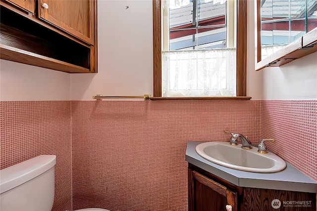 bathroom featuring vanity, a wainscoted wall, toilet, and tile walls