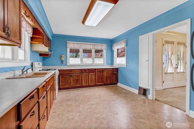 kitchen featuring open shelves, brown cabinets, a sink, light countertops, and white range with gas cooktop
