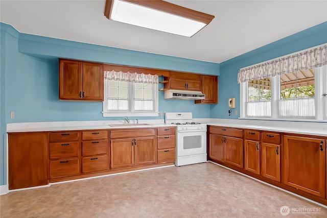 kitchen featuring brown cabinets, a sink, light countertops, white gas range, and under cabinet range hood