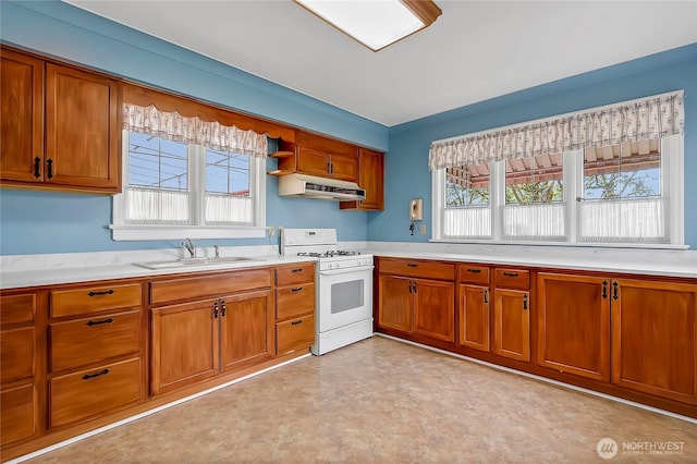 kitchen with brown cabinets, a sink, light countertops, white range with gas stovetop, and under cabinet range hood