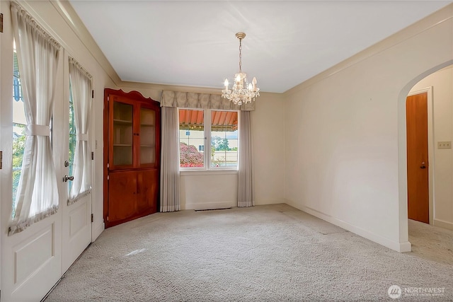 empty room with arched walkways, baseboards, a chandelier, and light carpet