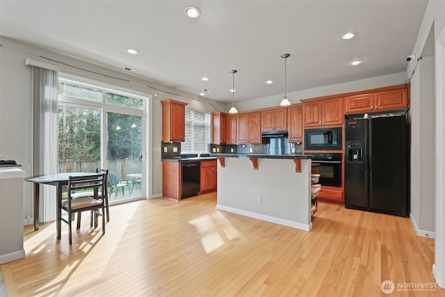 kitchen with dark countertops, a kitchen bar, light wood-type flooring, recessed lighting, and black appliances