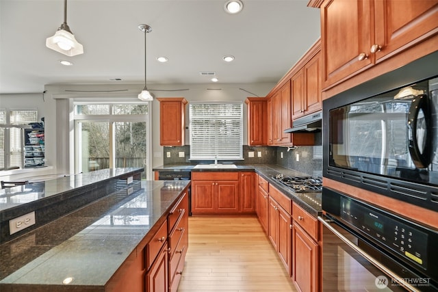 kitchen featuring hanging light fixtures, light wood-style flooring, backsplash, under cabinet range hood, and black appliances