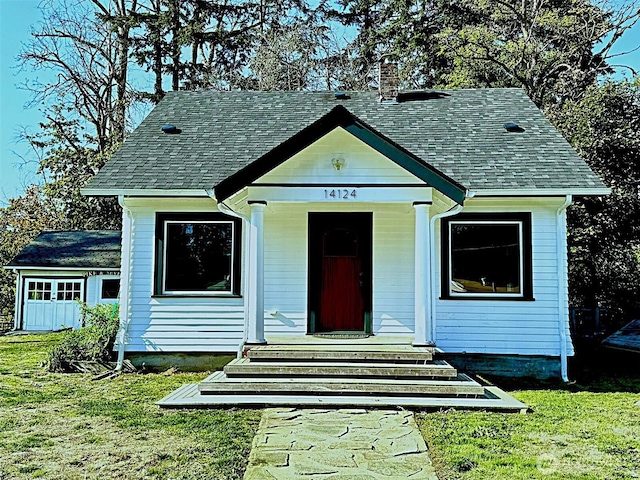 bungalow-style home with a chimney, a front yard, and a shingled roof