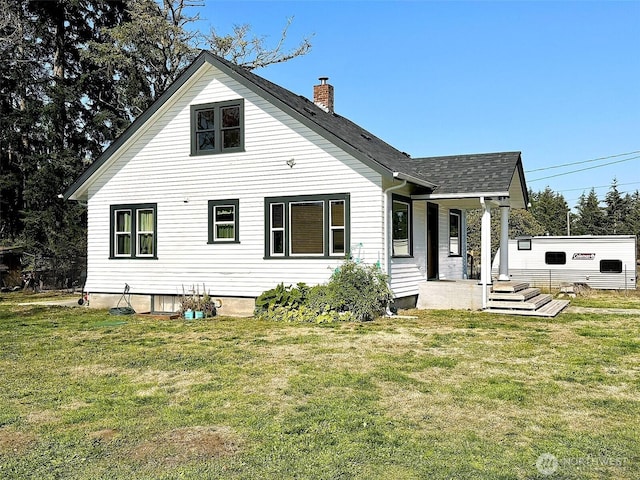 rear view of house featuring a chimney, a porch, a yard, and roof with shingles