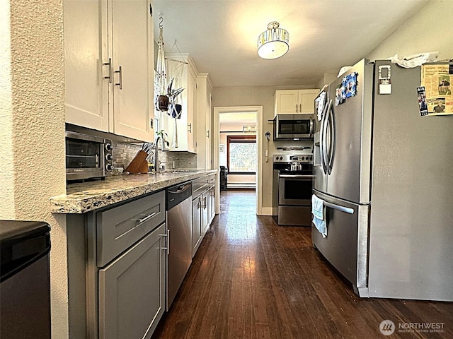 kitchen with stainless steel appliances, a sink, dark wood-style flooring, white cabinets, and tasteful backsplash