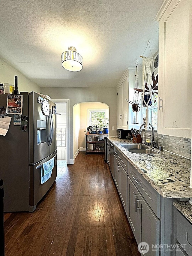 kitchen with stainless steel refrigerator with ice dispenser, a sink, arched walkways, dark wood-style floors, and gray cabinetry