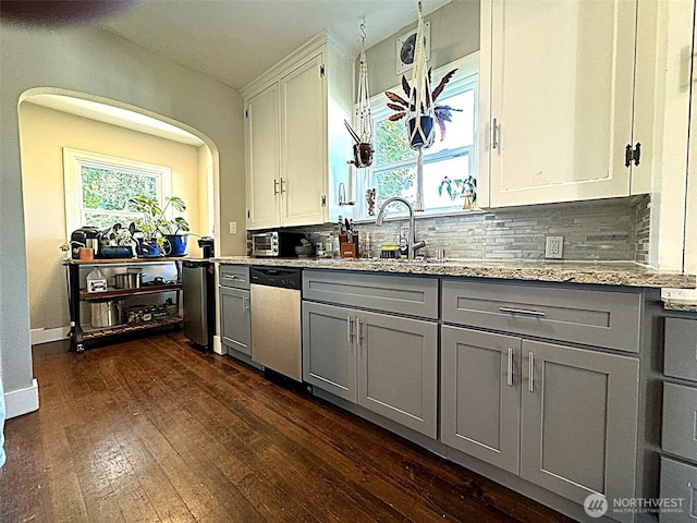 kitchen featuring gray cabinets, stainless steel dishwasher, a sink, tasteful backsplash, and dark wood finished floors