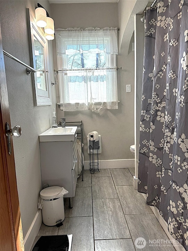 bathroom with baseboards, vanity, toilet, and curtained shower