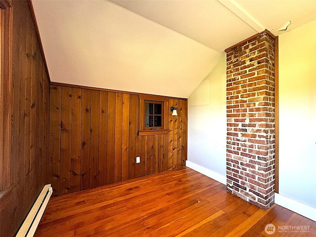 spare room with a baseboard heating unit, lofted ceiling, wood finished floors, wood walls, and baseboards
