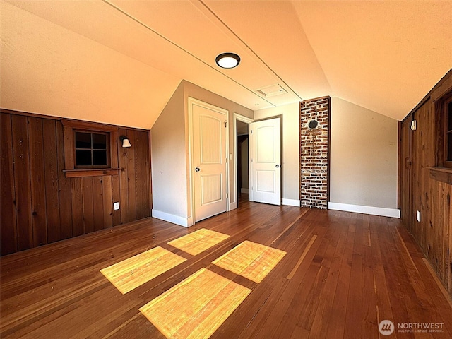additional living space with vaulted ceiling, wooden walls, hardwood / wood-style flooring, and baseboards
