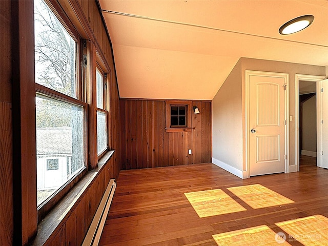additional living space with a baseboard radiator, hardwood / wood-style flooring, lofted ceiling, wood walls, and baseboards