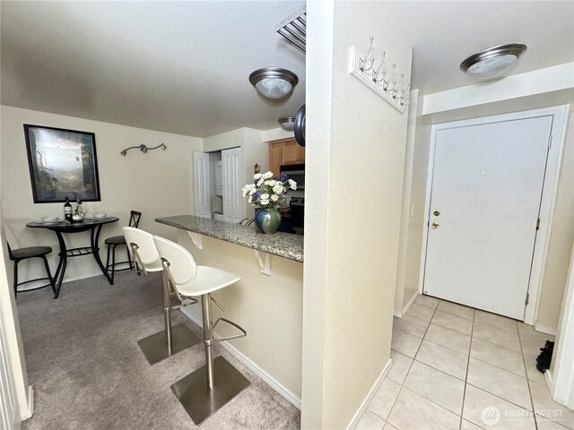 kitchen featuring a kitchen breakfast bar, black microwave, brown cabinets, light tile patterned floors, and baseboards