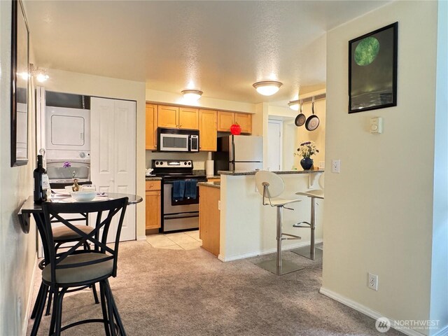 kitchen with appliances with stainless steel finishes, light carpet, stacked washing maching and dryer, a peninsula, and a kitchen bar