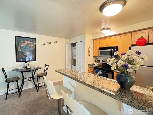 kitchen featuring light brown cabinetry, appliances with stainless steel finishes, a kitchen breakfast bar, carpet, and stone counters