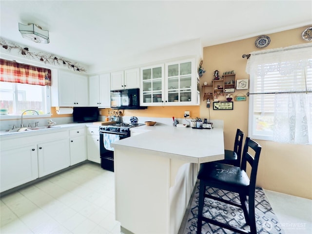 kitchen featuring a peninsula, a kitchen bar, a sink, range with gas stovetop, and black microwave