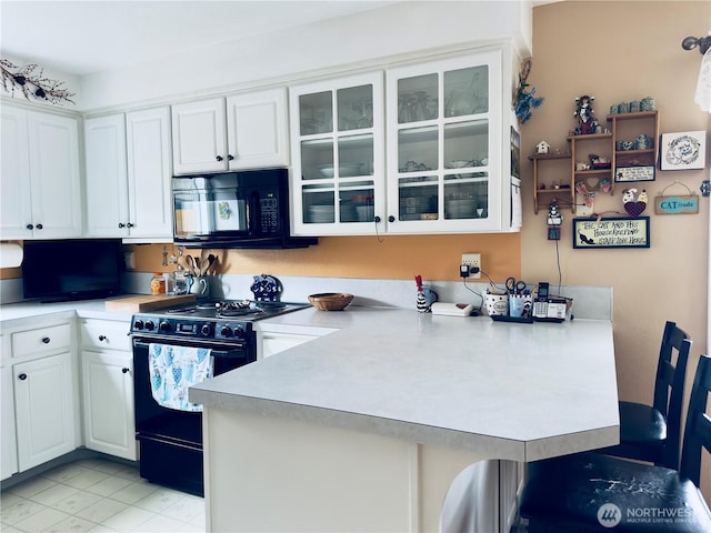 kitchen with a peninsula, glass insert cabinets, white cabinets, black appliances, and light countertops