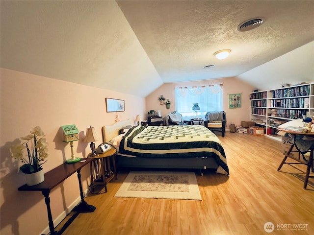 bedroom with lofted ceiling, visible vents, a textured ceiling, and wood finished floors