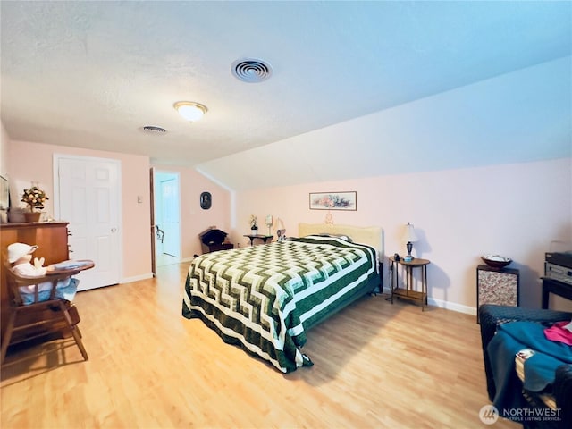 bedroom with light wood finished floors, visible vents, baseboards, and lofted ceiling