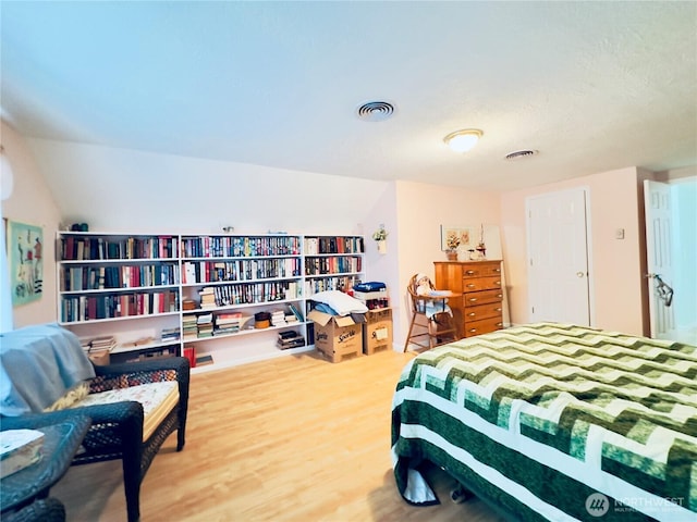 bedroom with vaulted ceiling, visible vents, and wood finished floors