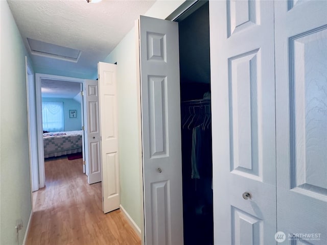 corridor featuring light wood-style flooring, attic access, and baseboards
