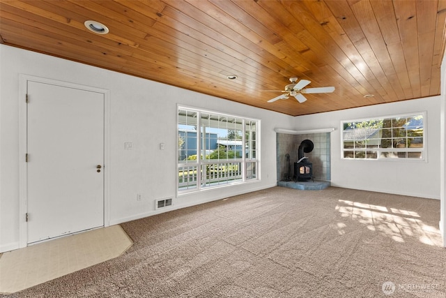 unfurnished living room featuring wood ceiling, plenty of natural light, and a wood stove