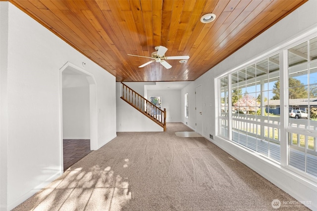 unfurnished living room with ceiling fan, carpet floors, arched walkways, stairs, and wood ceiling