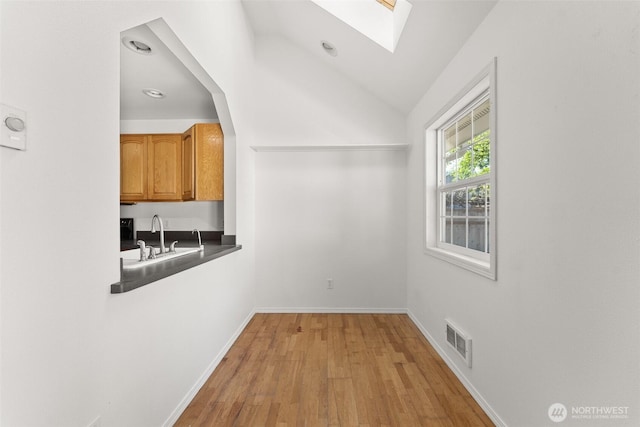 interior space featuring a sink, vaulted ceiling with skylight, baseboards, light wood-type flooring, and visible vents