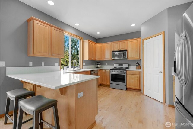kitchen with a peninsula, a kitchen breakfast bar, light wood-type flooring, a sink, and stainless steel appliances