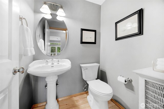 half bath with wood finished floors, a sink, baseboards, toilet, and radiator heating unit