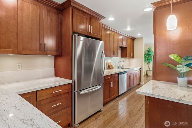 kitchen with brown cabinets, light stone counters, appliances with stainless steel finishes, a sink, and light wood-type flooring