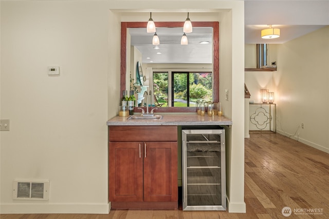 bar with visible vents, a sink, baseboards, beverage cooler, and light wood-style flooring