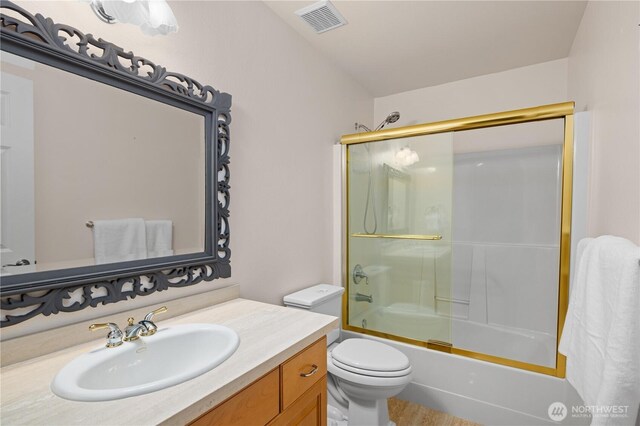 bathroom featuring toilet, visible vents, shower / bath combination with glass door, and vanity