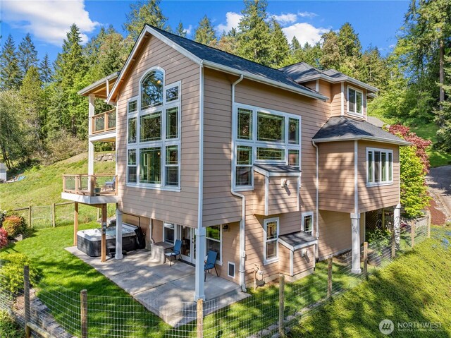 rear view of house with fence, a jacuzzi, a patio area, a balcony, and a yard