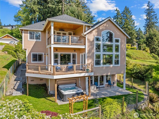 back of house featuring a balcony, a fenced backyard, a patio area, a lawn, and a hot tub